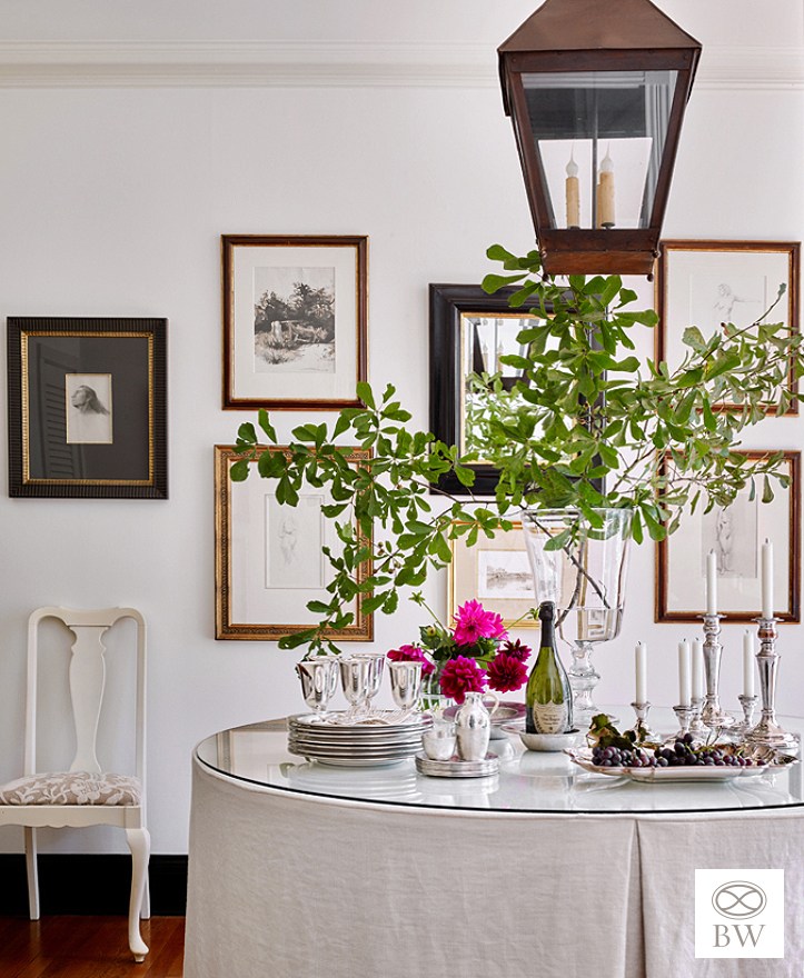 Elegant neutral entryway by Beth Webb featuring a classic round table with a linen inverted-pleat tablecloth, a hanging copper lantern, fresh leafy branches, and an effortlessly hung gallery wall
