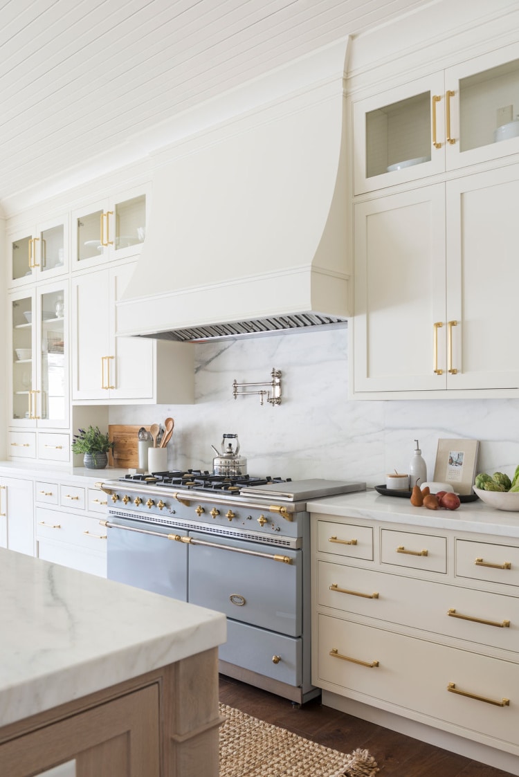 Beautiful Studio McGee kitchen with a Lacanche French range and marble countertops | Lucy Call Photography | kitchen | white kitchen | glass front cabinets | range hood | brass hardware | brass | la Jolla